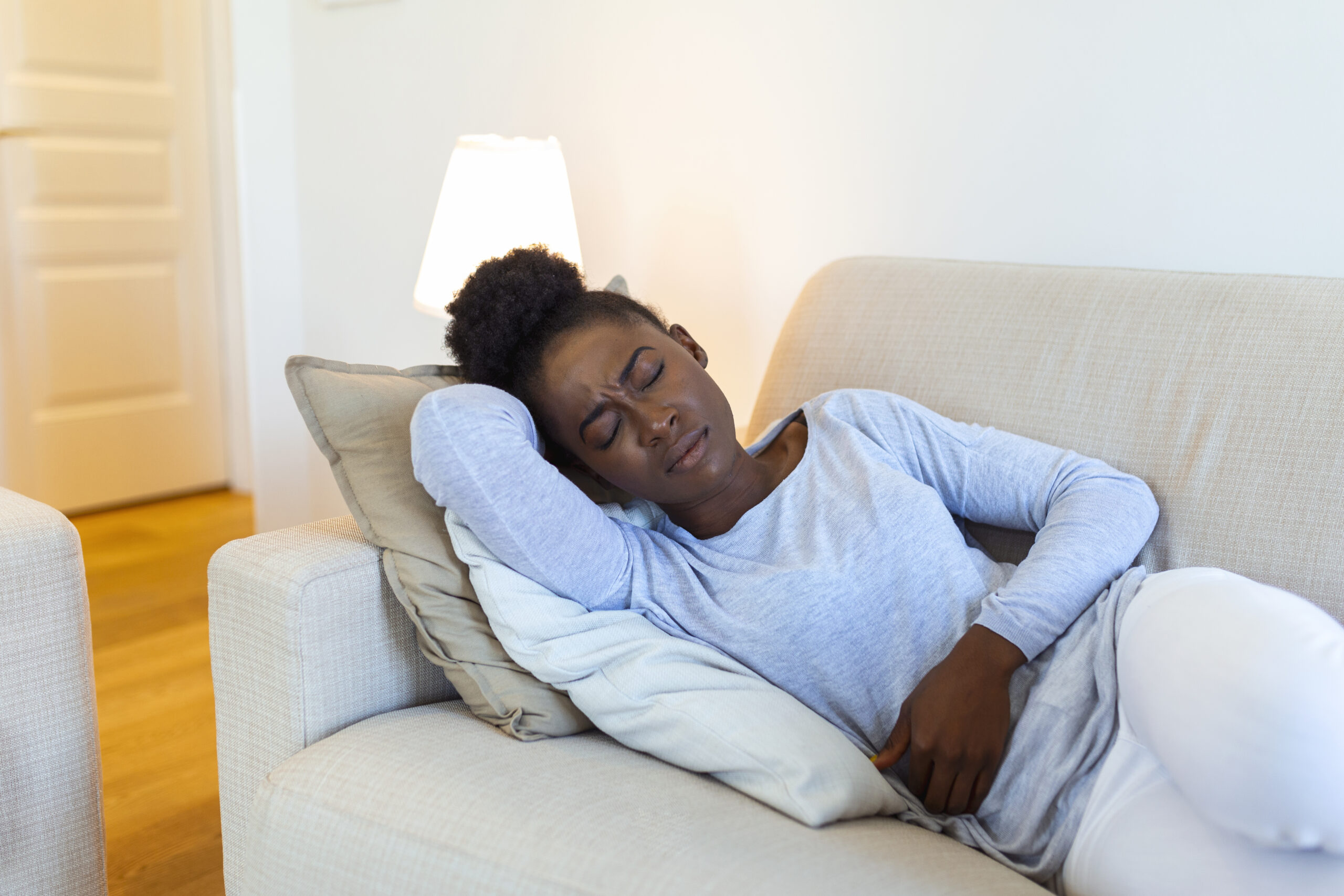 Woman lying on sofa looking sick in the living room. Beautiful young woman lying on bed and holding hands on her stomach. Woman having painful stomachache on bed, Menstrual period
